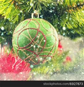 Green Christmas ball on a branch with stylized falling snow