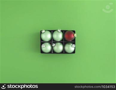 Green Christmas balls and just one red bauble in a black box on a green background. Xmas traditional decorations. Flat lay of Christmas ornaments.