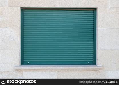 Green closed metal shutter on a window of a stone house
