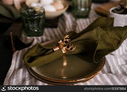Green cloth napkin is secured with a golden ring in the form of a deer’s head.