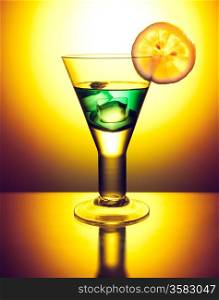 Green cocktail with ice decorated with a lemon slice on orange background