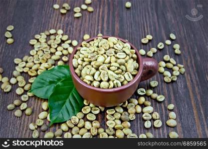 Green coffee beans in a brown cup and on a table with leaves on a wooden board background
