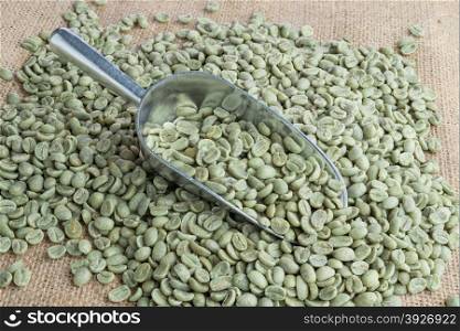 Green coffee beans in metal scoop on burlap surface