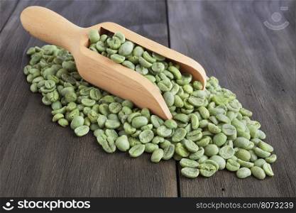 Green coffee beans in wooden scoop on vintage wooden surface