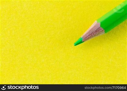 Green color pencil on yellow background color paper arranged diagonally. Minimalist composition.