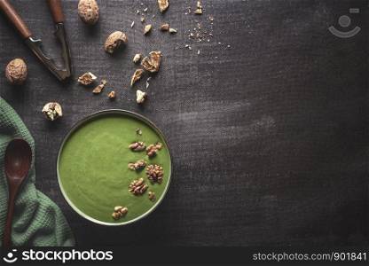 Green cream soup from fresh spinach and walnuts. Above view of vegetable soup bowl on a kitchen table. Flat lay of healthy dinner with copy space.