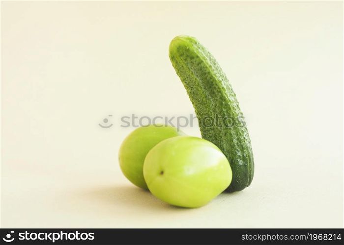 green cucumber and two green tomatoes on a beige background. male penis concept.