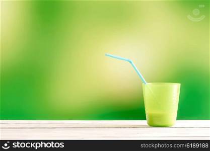 Green cup with a blue straw on a wooden table