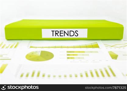 Green document binder with trends word place on graphs, charts and marketing reports