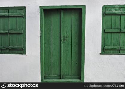 Green door wooden window shutters and white wall.