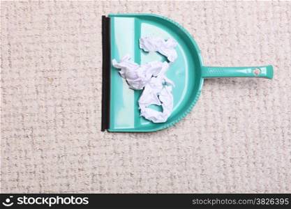 Green dustpan for house work with garbage papers on floor indoors. Cleaning