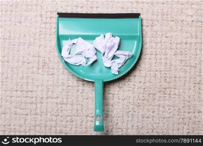 Green dustpan for house work with garbage papers on floor indoors. Cleaning