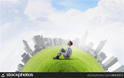 Green eco planet. Young smiling businessman sitting on green grass planet