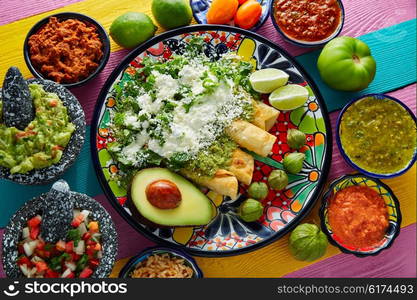 Green enchiladas Mexican food with guacamole and sauces on colorful table