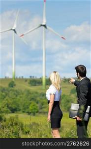 Green energy businesspeople - Young businesswoman pointing at windmill in field