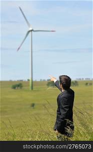 Green energy - Young businessman point at field windmill in background