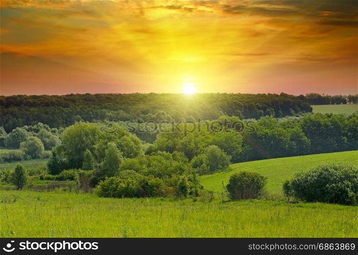 Green fields and bright sunrise over horizon. hills are covered with trees and shrubs.