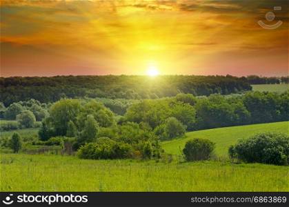 Green fields and bright sunrise over horizon. hills are covered with trees and shrubs.