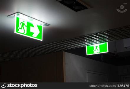 Green fire escape sign hang on the ceiling in the office at night.