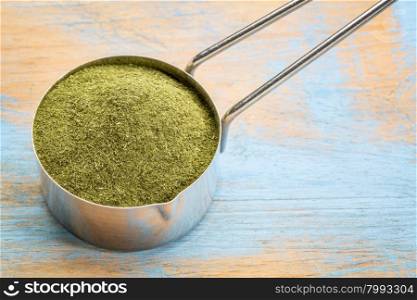 green freeze-dried organic wheat grass powder, nutritional supplement on a metal measuring scoop against painted grunge wood