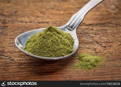 green freeze-dried organic wheat grass powder, nutritional supplement on a tablespoon against rustic wood