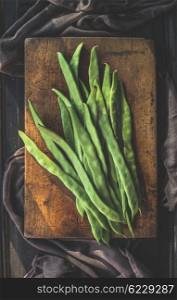 Green french beans on cutting board and dark wooden background, top view