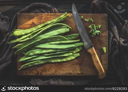 Green french beans on rustic cutting board with kitchen knife on dark wooden background, top view. Legumes vegetables