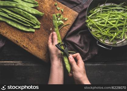 Green french beans, preparation on dark kitchen table. Woman Female hands cut beans with vegetable peeler. Cutting board with Green french beans and sliced beans , top view