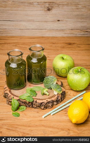 Green fresh leafy greens smoothie in glass jar, spinach leaves, apple, broccoli and lemon. Refreshing healthy drink on wooden table background