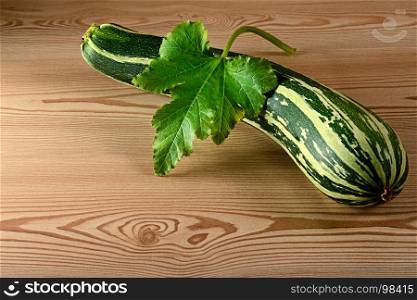 Green fresh zucchini with leaf on wooden table in kitchen. Top view. Free space for text.