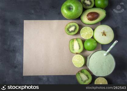 Green fruits and a glass with a smoothie, on an empty brown paper page, on a greyish background. Detox drink. Dieting context. Healthy eating.