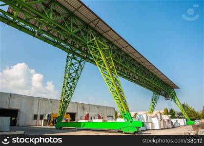 Green gantry crane at work in a warehouse of marble blocks