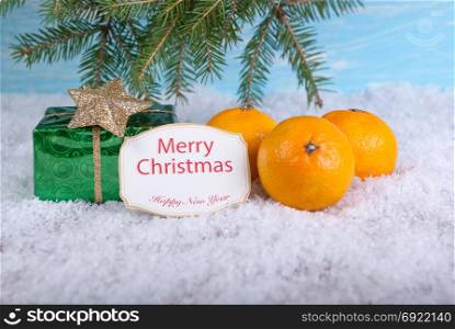Green gift box and three yellow mandarins on the snow and a greeting card.