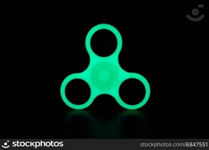 Green glowing in the dark fidget spinner on black background. Glowing in the dark fidget spinner