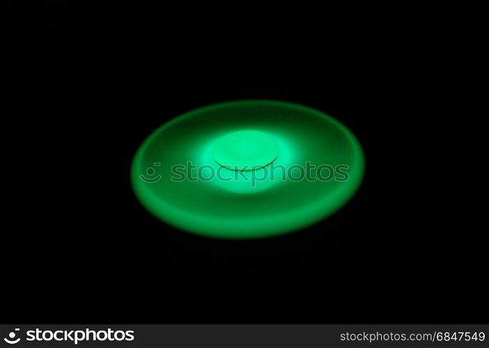 Green glowing in the dark fidget spinner spinning on black background. Glowing in the dark fidget spinner, rotating