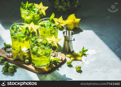 Green gooseberry and carambola cocktail with liqueur, ice and fresh mint on a light gray concrete table. Refreshing summer drink, sunny light. Or detox drink.