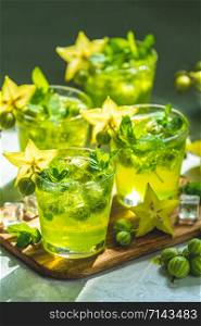 Green gooseberry and carambola cocktail with liqueur, ice and fresh mint on a light gray concrete table. Refreshing summer drink, sunny light. Or detox drink