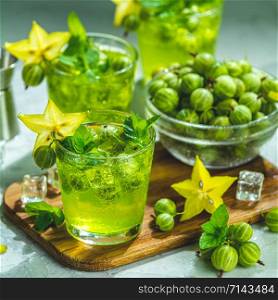 Green gooseberry and carambola cocktail with liqueur, ice and fresh mint on a light gray concrete table. Refreshing summer drink, sunny light. Or detox drink.