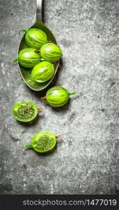Green gooseberry in a spoon. On a stone background.. Green gooseberry in a spoon. On stone background.