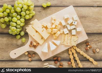 green grapes almonds bread sticks cheese blocks chopping board wooden desk
