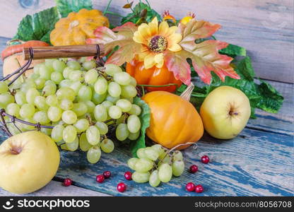 Green grapes in a basket and ripe apples, red cranberries, orange decorative pumpkin and squash with leaves on the wooden background