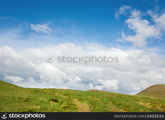 green grass covered summer mountainside, footway and cloudy sky