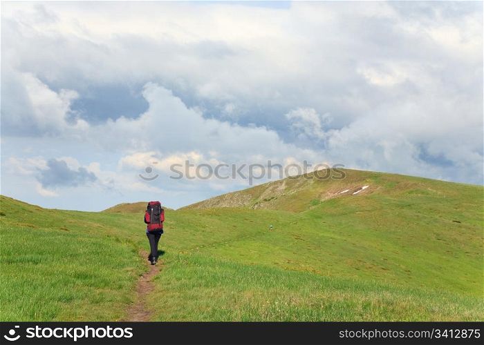 green grass covered summer mountainside, tourist on footway and cloudy sky
