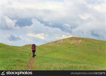 green grass covered summer mountainside, tourist on footway and cloudy sky