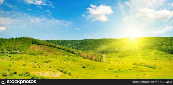 Green grass field on small hills and sun on blue sky . Wide photo.