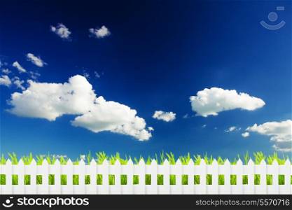 Green grass over blue sky and white fence