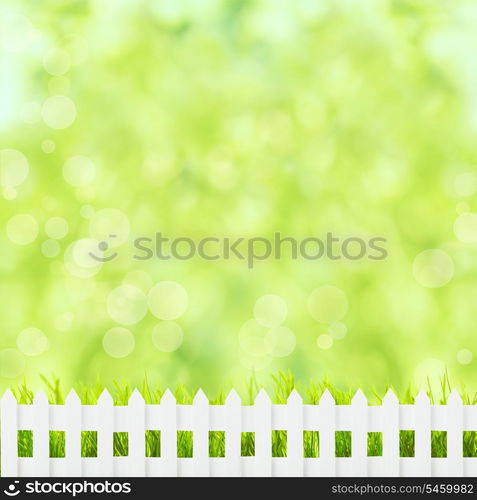 Green grass over spring bokeh and white fence