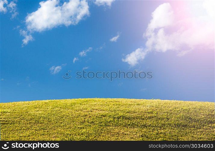Green grassy lawn or meadow with blue sky and sun flare. Bright green sunlit grass hill with blue sky and clouds with sun flare and copy space. Green grassy lawn or meadow with blue sky and sun flare