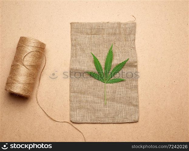 green hemp leaf, skein with brown rope and empty bag on a brown wooden background, concept of rejection of plastic packaging, zero waste