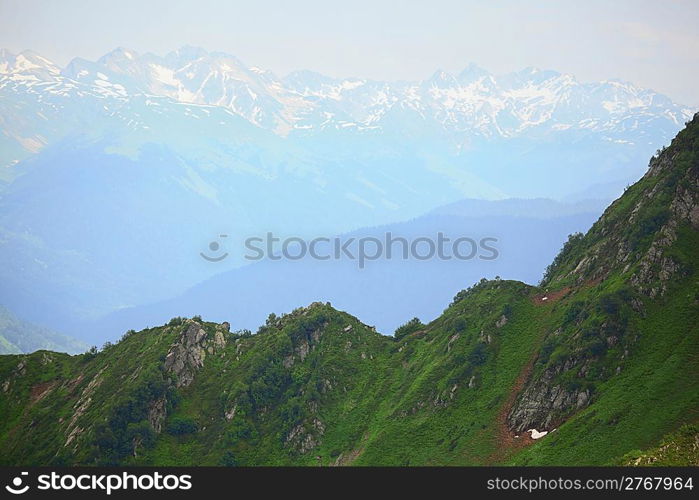 green hillside. mountains with snow caps in the distance.